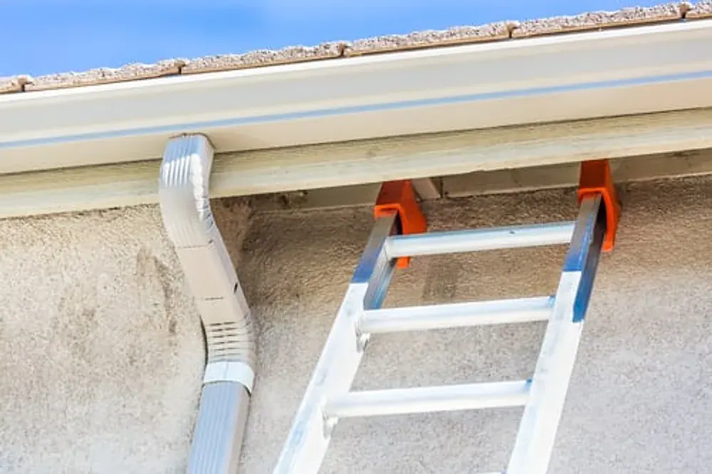 Ladder set against a home's gutter and downspout for cleaning