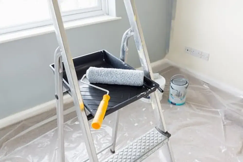 Paint roller, tray and ladder set up in a room being repainted