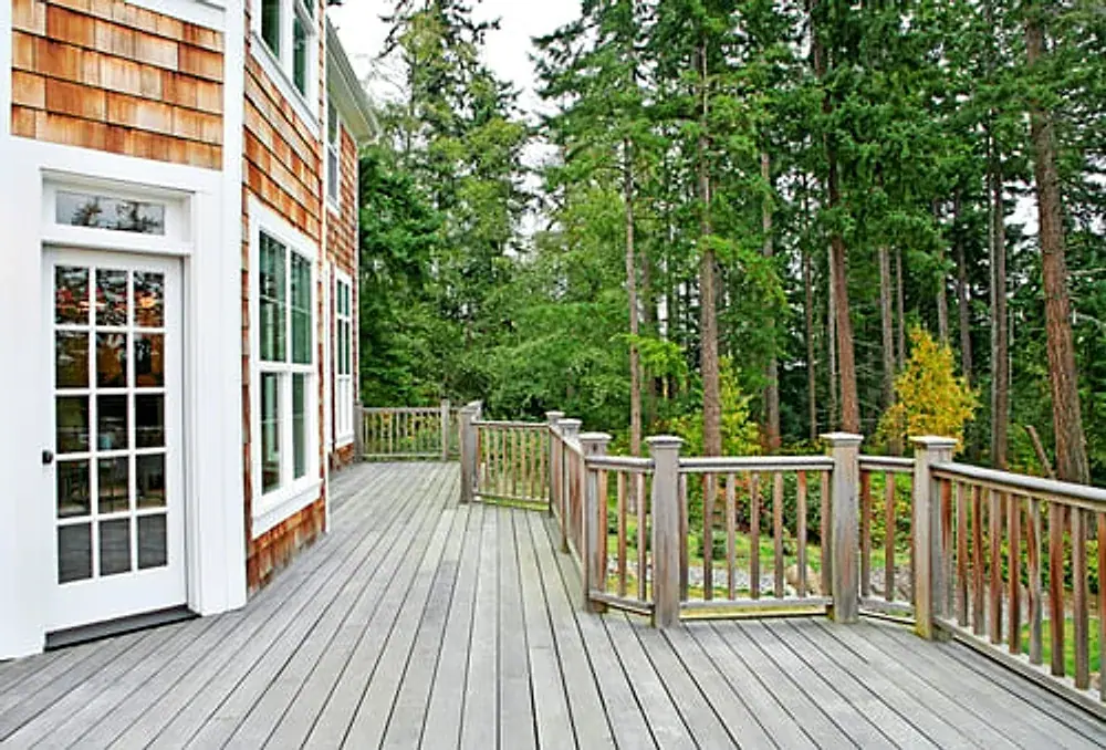Wood deck with railing alongside a shingled home surrounded by trees