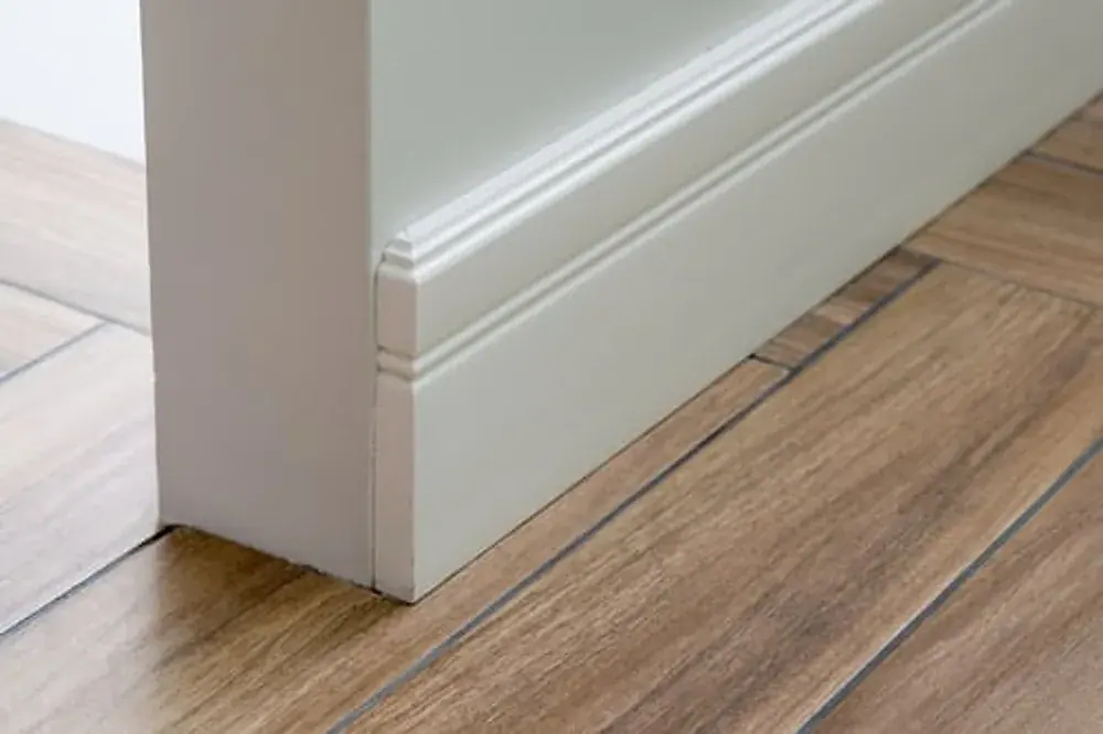 Freshly installed painted door casing meeting baseboard on wood flooring